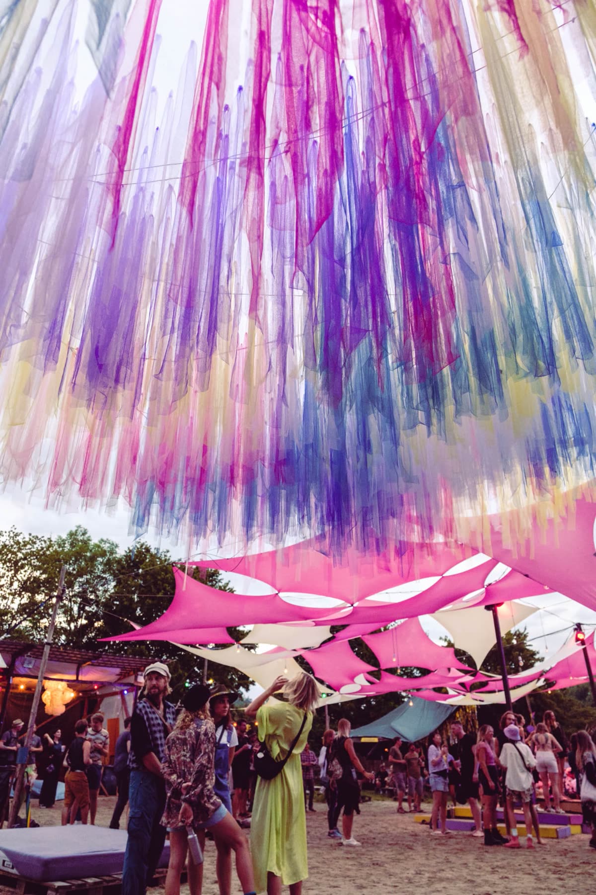 Bunte Bänder hängen über einem Festivalplatz mit rosa Sonnensegeln